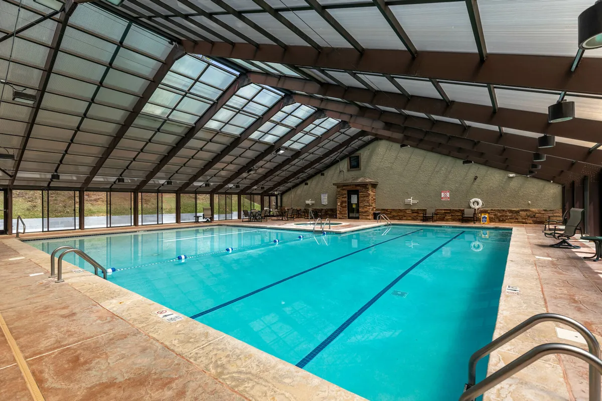 An indoor swimming pool surrounded by large glass windows that let in natural light, with a stone accent wall adding to the mountain lodge vibe. The space feels both luxurious and calming, ideal for relaxing swims or social gatherings.