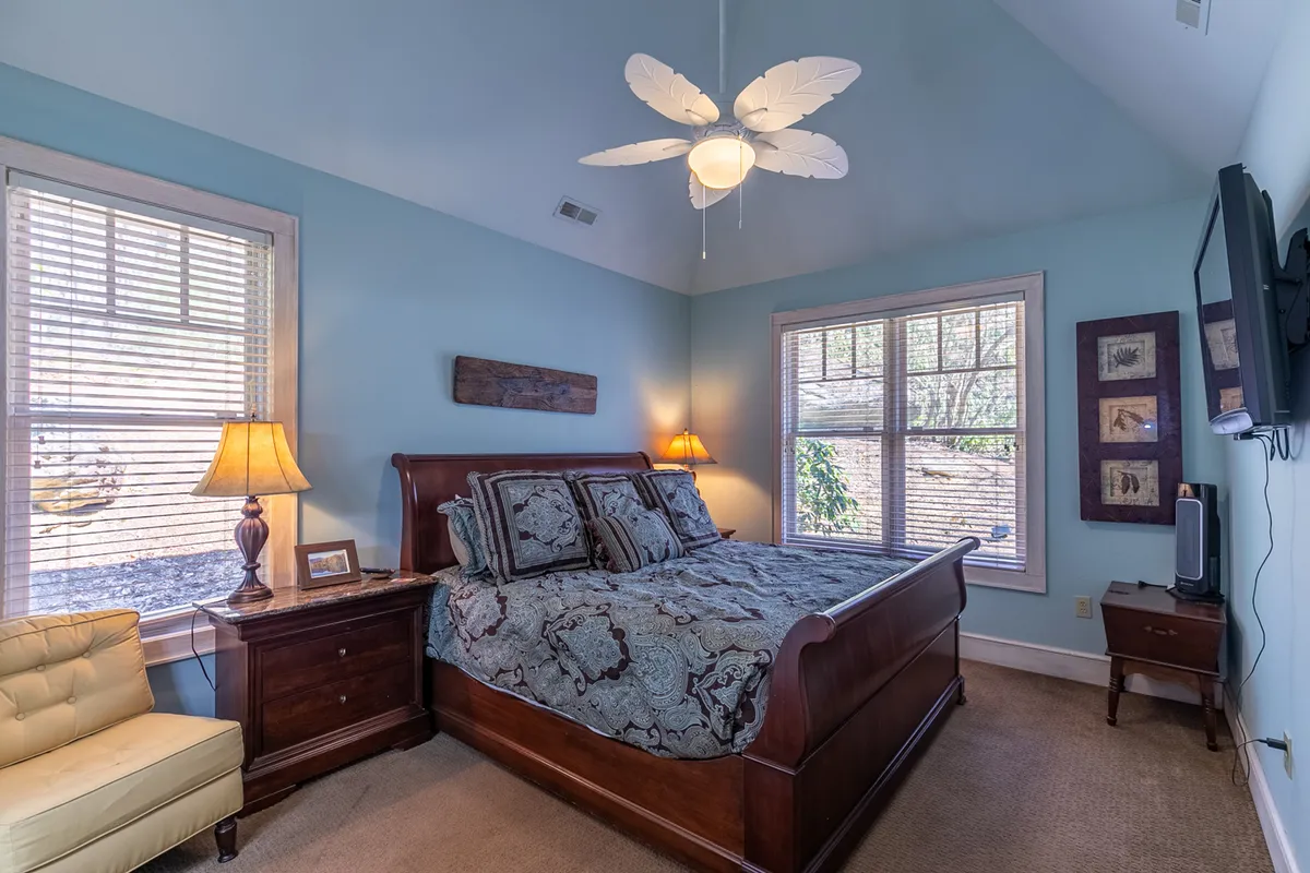 A tranquil bedroom featuring a comfortable bed, bedside lamps, a window letting in natural light, and a ceiling fan overhead. The décor is calming and the space feels restful, ideal for a master or king suite retreat.