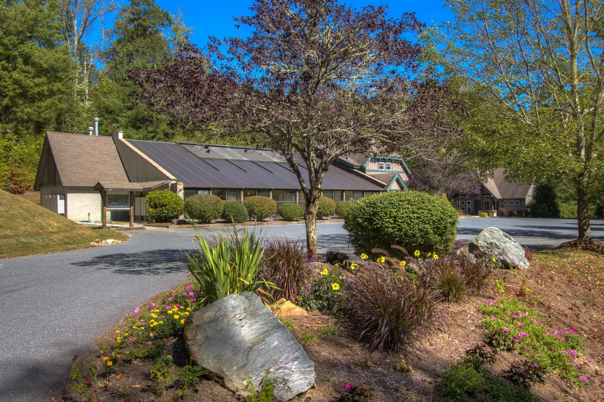 A beautifully landscaped exterior with vibrant flower beds, meticulously maintained shrubs, and a building topped with solar panels. The outdoor scene conveys a sense of community and sustainability, with open space hinting at areas for gatherings or relaxation.