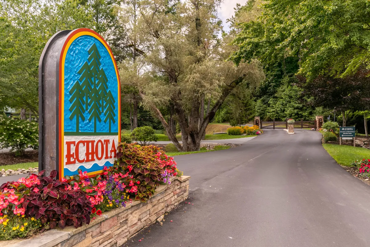 This image captures the Echota community sign surrounded by lush greenery and colorful flower beds, providing a welcoming sense of arrival. A pathway suggests opportunities for walking and exploring the beautifully landscaped entrance.