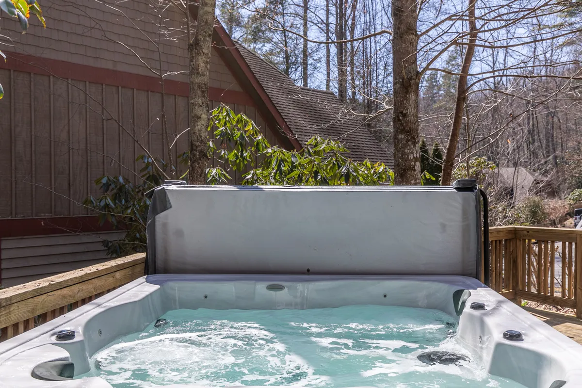 A spacious wooden deck nestled among trees features a private hot tub, providing a relaxing space to unwind and take in the serene surroundings. The deck’s positioning highlights the indoor-outdoor living experience.