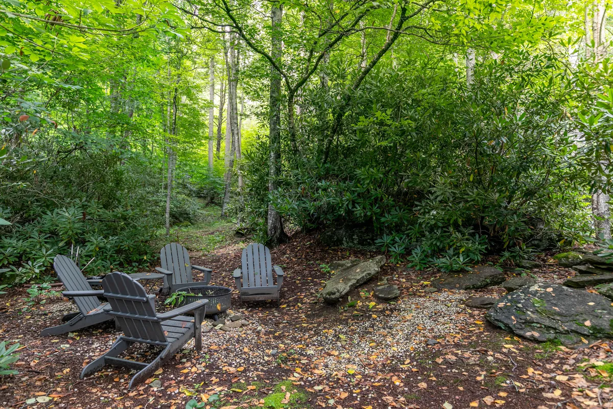 A cozy fire pit area with classic Adirondack chairs encircling a glowing fire, set against a backdrop of verdant greenery. The intimate arrangement invites gatherings for stories and s’mores under the stars.