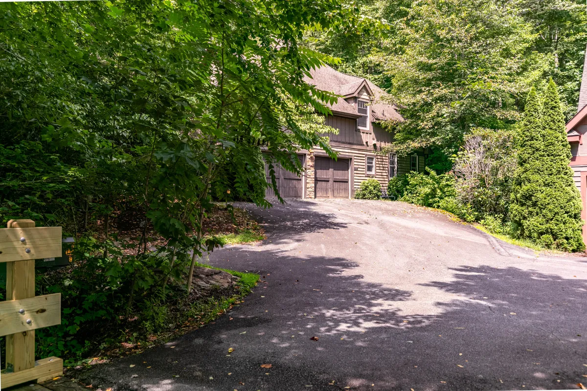 This exterior shot features the mountain retreat itself, nestled among tall trees with a gently curving driveway leading to the home. The landscape radiates tranquility, with inviting spaces for families to gather outdoors, enjoy morning coffee on the porch, or explore the natural surroundings.