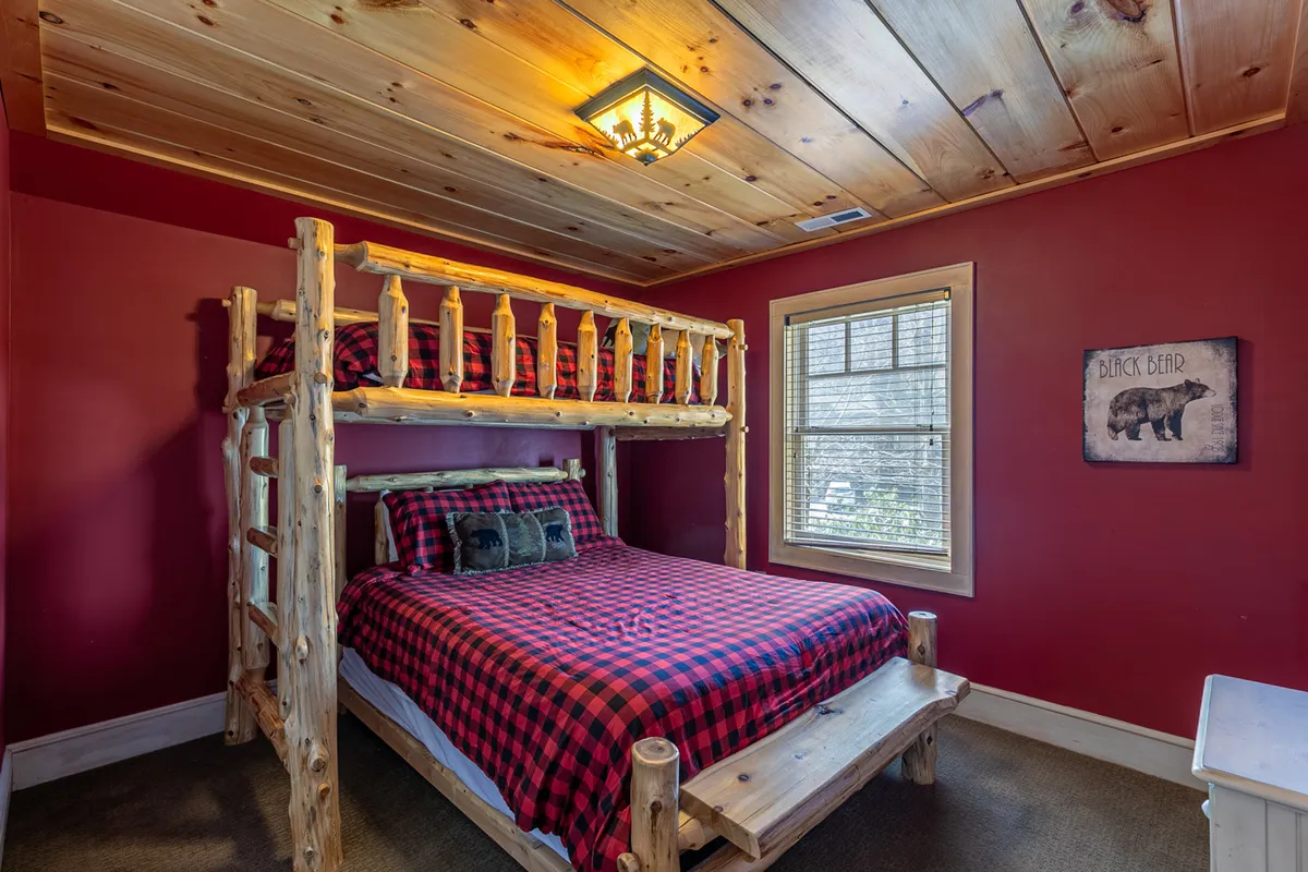 A cozy bunk bedroom with a twin-over-queen bunk bed dressed in plaid bedding, playful wall art featuring a bear, and warm wooden accents. Sunlight filters in, creating a bright, family-friendly atmosphere.