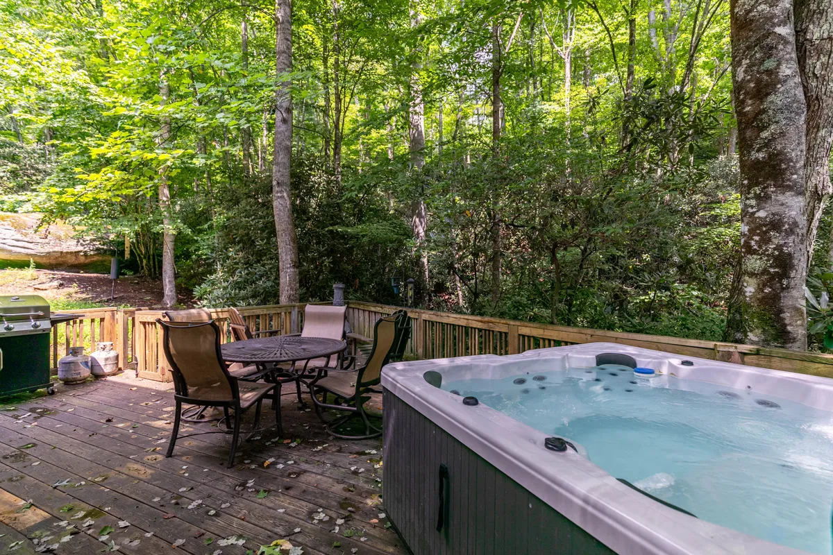 A private outdoor deck with a bubbling hot tub and comfortable seating overlooks the surrounding forest. The tranquil space invites guests to relax under the stars or gather for conversations in a peaceful, natural setting.